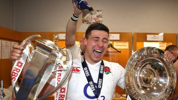 Ben Youngs smiles with two trophies as someone pours champagne on his head