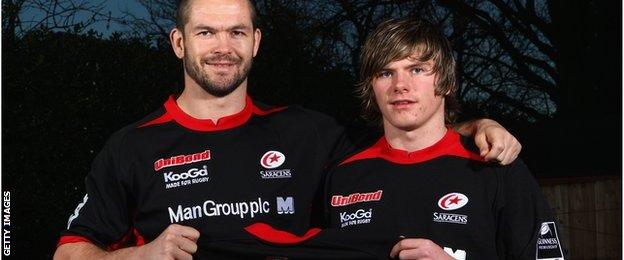 Andy Farrell has his arm round a young Owen Farrell and both are holding a Saracens shirt with Farrell on the back